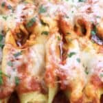 Close-up of baked stuffed pasta shells with melted cheese and fresh herbs in marinara sauce.